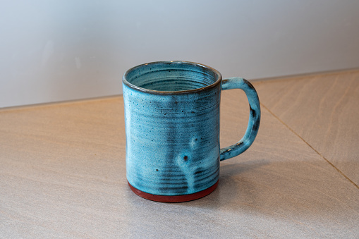 Handmade glazed blue coloured ceramic mug made on the potter's wheel, as a hobby, shot on a gray kitchen counter.
