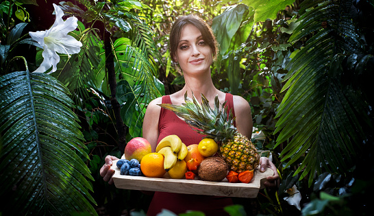 Woman holding a exotic fruit basket in the tropical garden