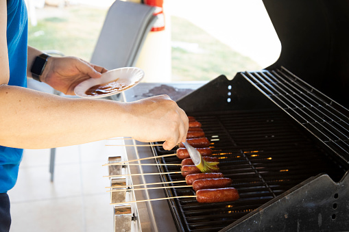 Caucasian man seasoning sausages as they cook on the barbecue in summer