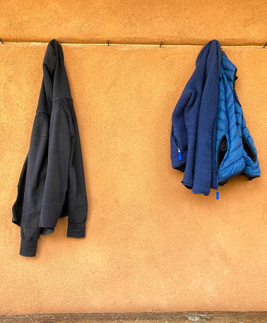 Two Jackets Hanging on Pegs on Orange Wall