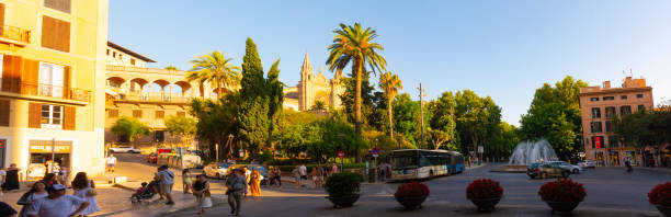Palma, Mallorca, Balearic Islands, Spain. July 21, 2022 - Panorama of the Plaza de la Reina, or Square of the Queen, with the Palma Cathedral in the background, behind the gardens, and street life
