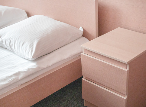 Soft pink tinting, close-up of the bed and bedside table, modern interior of the bedroom in the hotel.