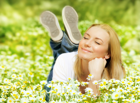 Beautiful woman enjoying daisy field, nice female lying down in the meadow of flowers, pretty girl relaxing outdoor, having fun, happy young lady and spring green nature, harmony and freedom concept