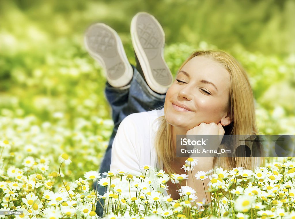 A woman laying in a field of wild flowers Beautiful woman enjoying daisy field, nice female lying down in the meadow of flowers, pretty girl relaxing outdoor, having fun, happy young lady and spring green nature, harmony and freedom concept Active Lifestyle Stock Photo