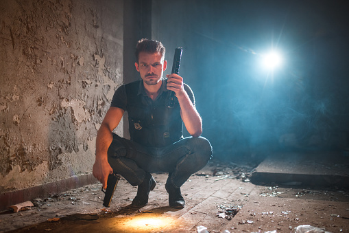 Portrait of a Caucasian male criminalist. He is searching for clues of a murder case. He is wearing a bullet proof vest and holding a fire gun.