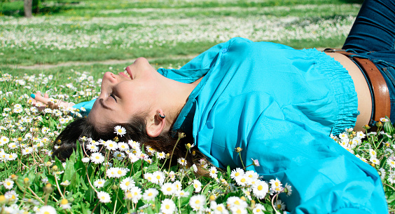 Beautiful young woman with marguerite lying on green grass in park. Freedom and calm concept