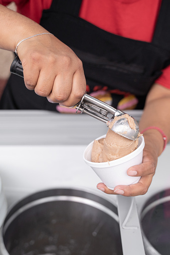 An Hispanic adult woman is serving nut ice cream on a cup in the street. Concept of traditional Mexican dessert