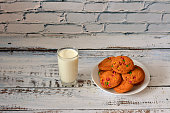 A glass of hot milk is on the table and a plate of several oatmeal cookies with multi-colored icing.