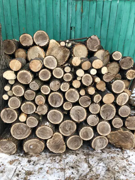 Photo of The background consists of sawn square wooden beams stacked on top of each other in the form of a woodpile near the wooden wall of the barn. Annual rings are visible on the cross-section of the trunks.