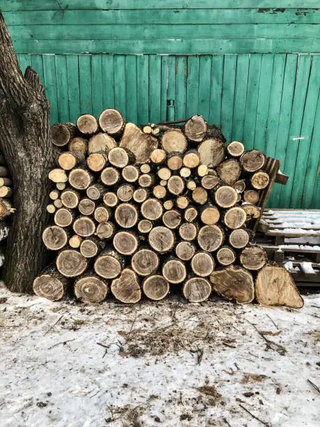 Photo of The background consists of sawn square wooden beams stacked on top of each other in the form of a woodpile near the wooden wall of the barn. Annual rings are visible on the cross-section of the trunks.