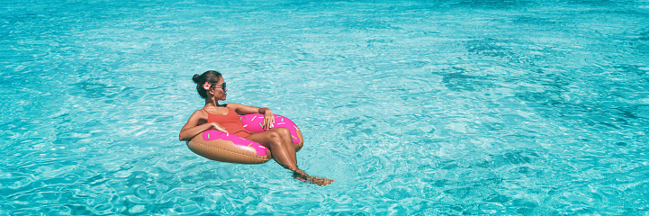Vacation beach banner woman relaxing on donut inflatable float ring swimming in turquoise ocean water panoramic. Summer travel sun lifestyle.