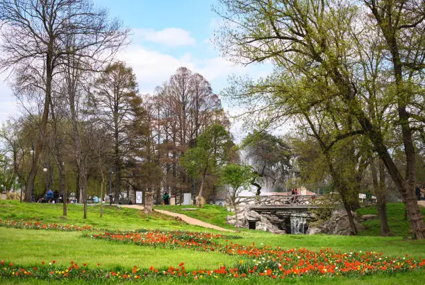 A beautiful park with many flowers and a bridge over the river.