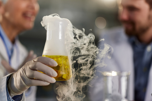 Close up of a female scientist examining yellow liquid with chemical reaction in laboratory.