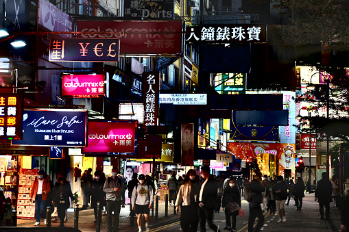 People walking on the sidewalks by night in Causeway Bay, beneath colourful neon placards, Hong Kong Island.