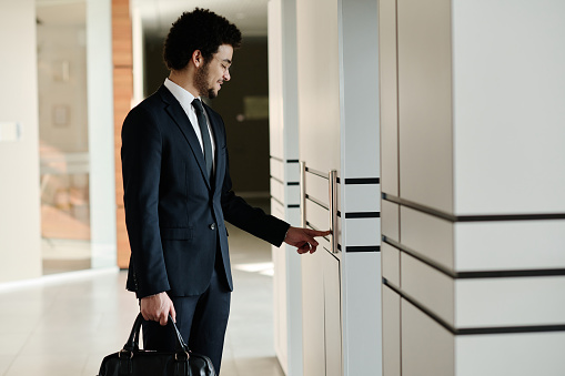 Young businessman in suit with briefcase using elevator standing in corridor of office building