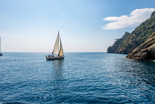 White sailing boat in motion in the blue Mediterranean sea (Ligurian sea) in front of the San Fruttuoso bay between Portofino and Camogli, Genoa province (Genova), Liguria, Italy, Europe.