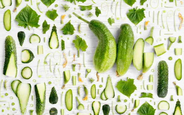 Abstract background made of Cucumber vegetable pieces, slices and leaves on wooden background.