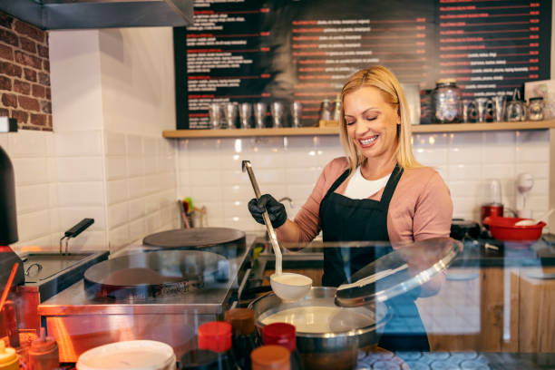 A smiling pancake shop worker is making crepes in a kitchen.