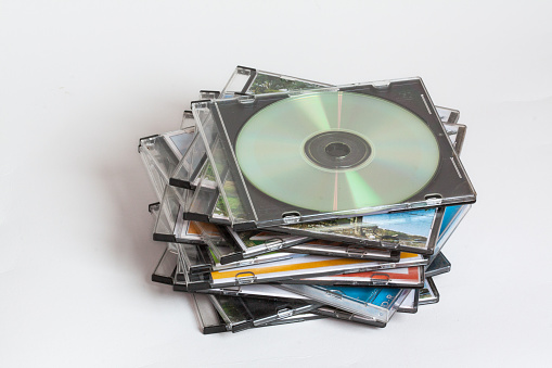 Group of compact discs in their cases stacked on top of each other on a white background
