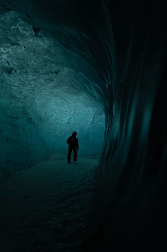 A man stands in an awe-inspiring and mysterious dark ice cave illuminated by a faint light