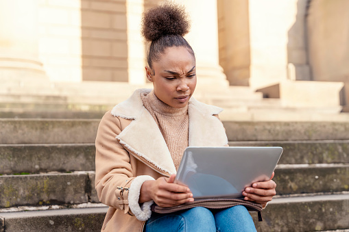 Upset woman student e-learning distance training course study working on stairs in the city. Multiethnic young woman watching online education webinar using a laptop