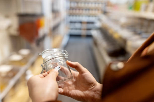 Cropped shot of a woman labelling a container at zero waste store. Close-up of a woman customer putting a label on container at eco-friendly shop.