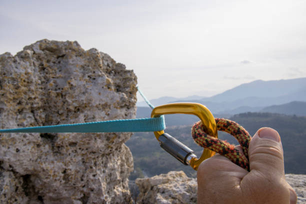 Hands attach rope to carabiner on mountain summit Maritime Alps, Liguria carabiner stock pictures, royalty-free photos & images