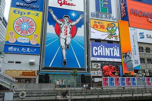 Osaka, Japan - March 21, 2023: Tourists taking photos in front of the famous Glico Man illuminated sign in Dotonbori, Osaka, Japan.