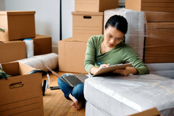 istock Asian woman going through checklist while using laptop and moving into a new home. 1481852533