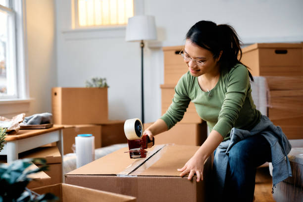 istock Asian woman taping carboard boxes while relocating into a new home 1481852585