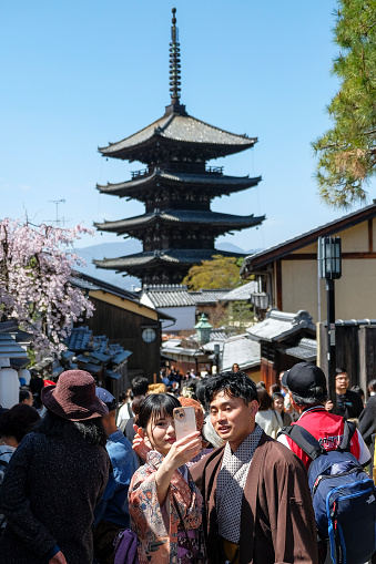 Kyoto, Japan - March 28, 2023: A couple dressed in kimonos take a selfie on Sannenzaka, a cobbled pedestrian street in Kyoto, Japan.
