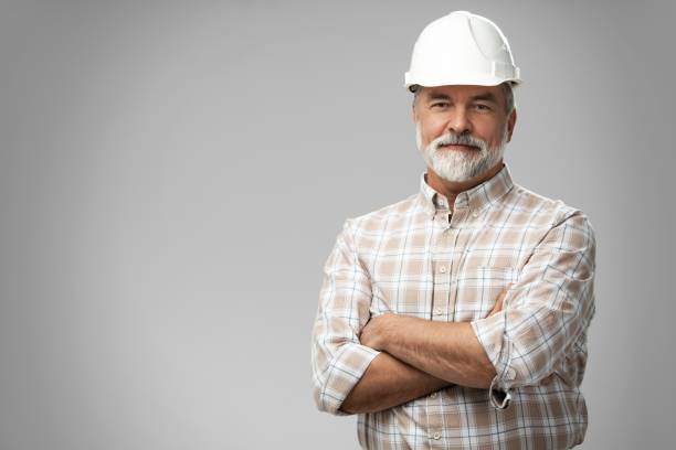 retrato de arquitecto maduro feliz con casco de pie con los brazos cruzados. inspector industrial de los años 50 posando en un estudio - construction worker architect construction manual worker fotografías e imágenes de stock