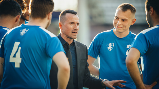 Professional Football Team Training, Tactical Coaching: Soccer Manager Explains Game Strategy, Workout Plan. Trainer Motivates Athletes, Lead to Victory, Preparing For Championship. Medium Shot.