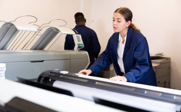 istock Focused young woman in uniform setting up the plotter before starting work in the printing house 1481858415