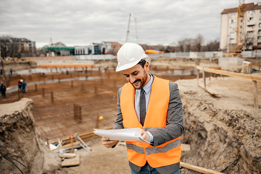 business, building, teamwork, gesture and people concept - group of smiling builders in hardhats with clipboard greeting each other outdoors