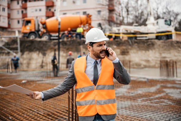 A nervous site manager is arguing with constructors on the phone while standing on site. The works aren't on time.
