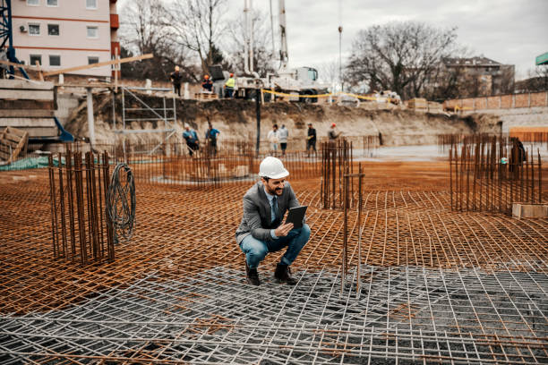 kierownik budowy kuca na fundamencie budynku i sprawdza prace podczas przewijania na tablecie. - crane mobile crane derrick crane construction vehicle zdjęcia i obrazy z banku zdjęć