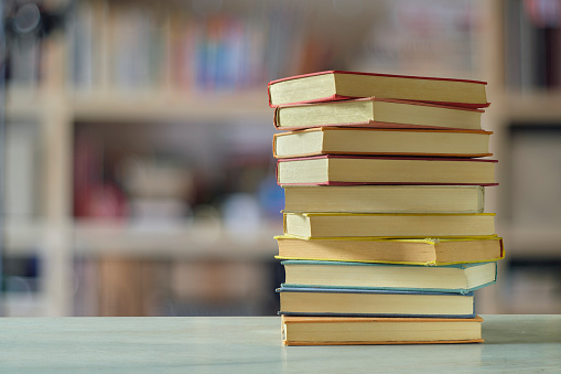 Stack of books with blurred bookshelf background, reading, learning, education or home office concept