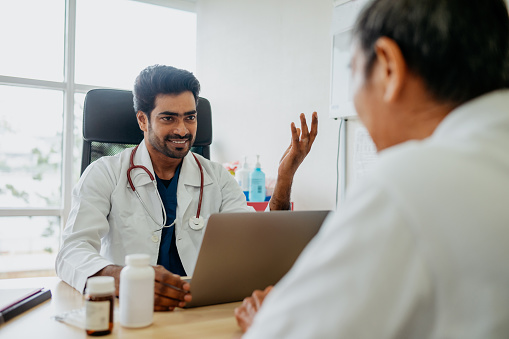 An Asian Indian doctor consulting a senior man patient in clinic. Doctor explaining medical report to his patient.