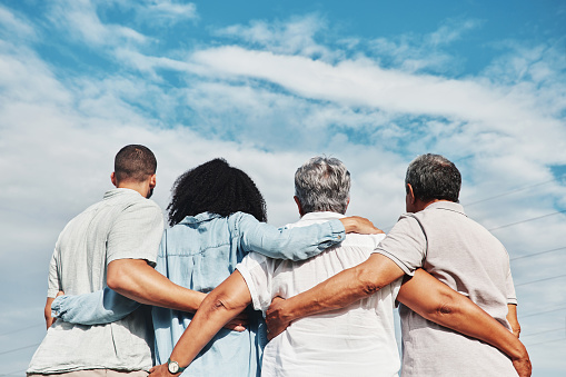 Family, back and hug of mom, grandparents and man together outdoor by blue sky. Love, care and senior people looking at view in nature feeling happiness and joy from travel for holiday in summer