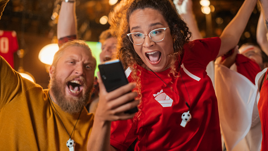 Excited Female Holding a Smartphone, Nervous About the Sports Bet She Put on a Her Favorite Soccer Team. Ecstatic Emotions When Football Team Scores a Goal and She Wins a High Stakes Lottery Prize.