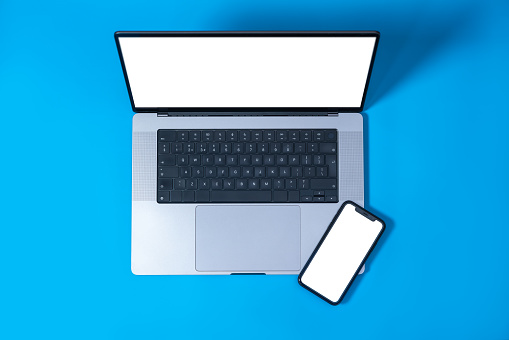 Laptop and smartphone with blank white screen isolated on blue background. Screen mockup