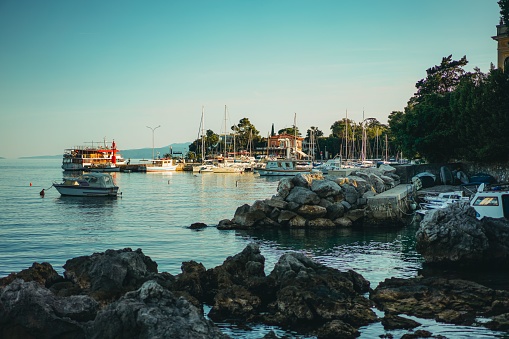 Opatija, Croatia – September 22, 2021: Three boats are docked in the port of Opatija, Croatia, situated against the stunning rocky shoreline of the Adriatic Sea