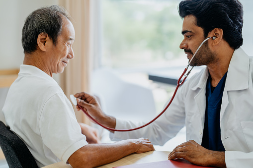 Image of an Asian Indian doctor examining senior man patient with a stethoscope in clinic