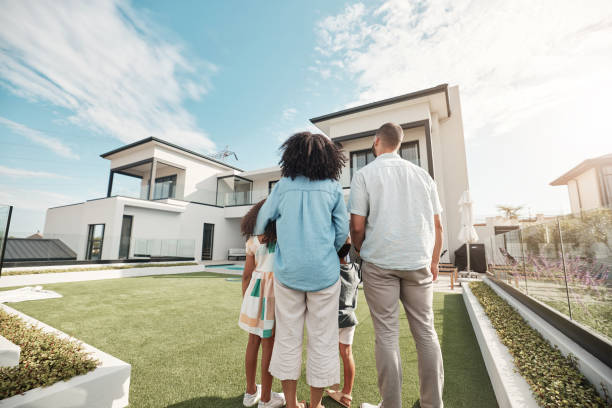 Love, new house and family in their backyard together looking at their property or luxury real estate. Embrace, mortgage and parents with their children on grass at their home or mansion in Canada. stock photo