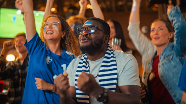 istock Soccer Club Members Cheering for Their Team, Playing in an International Cup Final. Supportive Fans Standing in a Bar, Cheering, Raising Hands and Shouting. Friends Celebrate Victory After the Goal. 1481869433