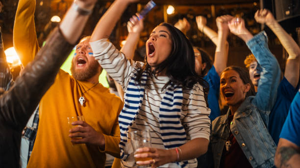 istock Soccer Club Members Cheering for Their Team, Playing in an International Cup Final. Supportive Fans Standing in a Bar, Cheering, Raising Hands and Shouting. Friends Celebrate Victory After the Goal. 1481869497