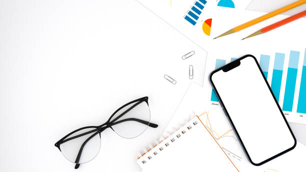 istock Office desk workplace with notepad, charts, smartphone, glasses and pencils on a white table. Top view. 3d rendering. 1481872356