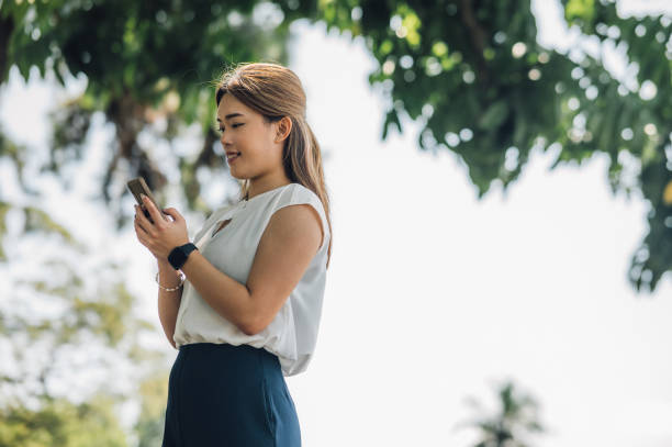 istock Balancing Technology and Nature: A Happy Asian Woman's Experience Reading Messages in a Public Par 1481872947