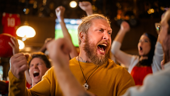 Excited Soccer Club Members Cheering for Their Team in a Pub. Supportive Fans Standing in a Bar, Cheering, Raising Hands and Shouting. Friends Celebrate Victory After the Goal.